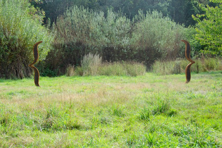 The artwork Breathing Space I at Anne Hathaway's Cottage. Two brackets, cast in a material that looks like rusted iron, are embedded in an area of open grass. The brackets are approximately 1.5m high and space about 5m apart.