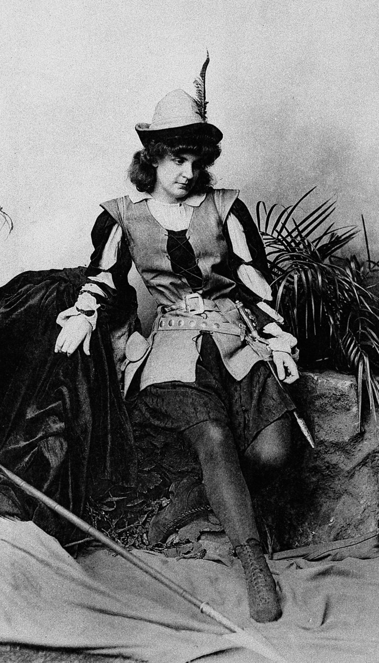 Ada Rehan as Rosalind, Lyceum Theatre, 1890 In male dress (tunic, knee-length breeches, stockings and boots), and wearing a hat with a feather over her short curly hair, Rosalind leans against a bank (cloth covered) and looks unseeing half-left.