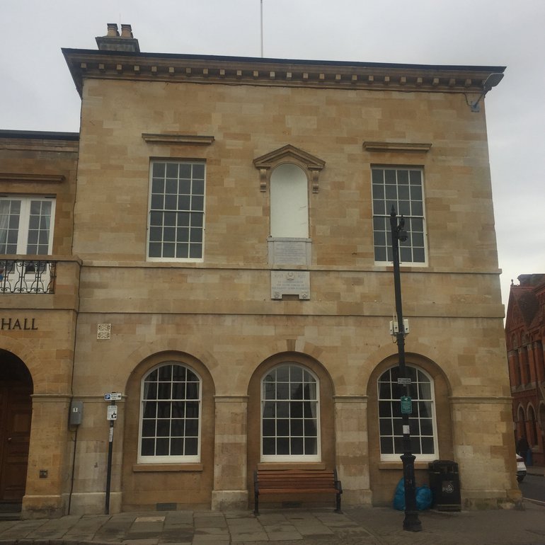 The yellow stone exterior of Stratford-upon-Avon Town Hall. It is a two-storey building. There is an empty niche which will be occupied by the statue of Shakespeare once restoration is complete.