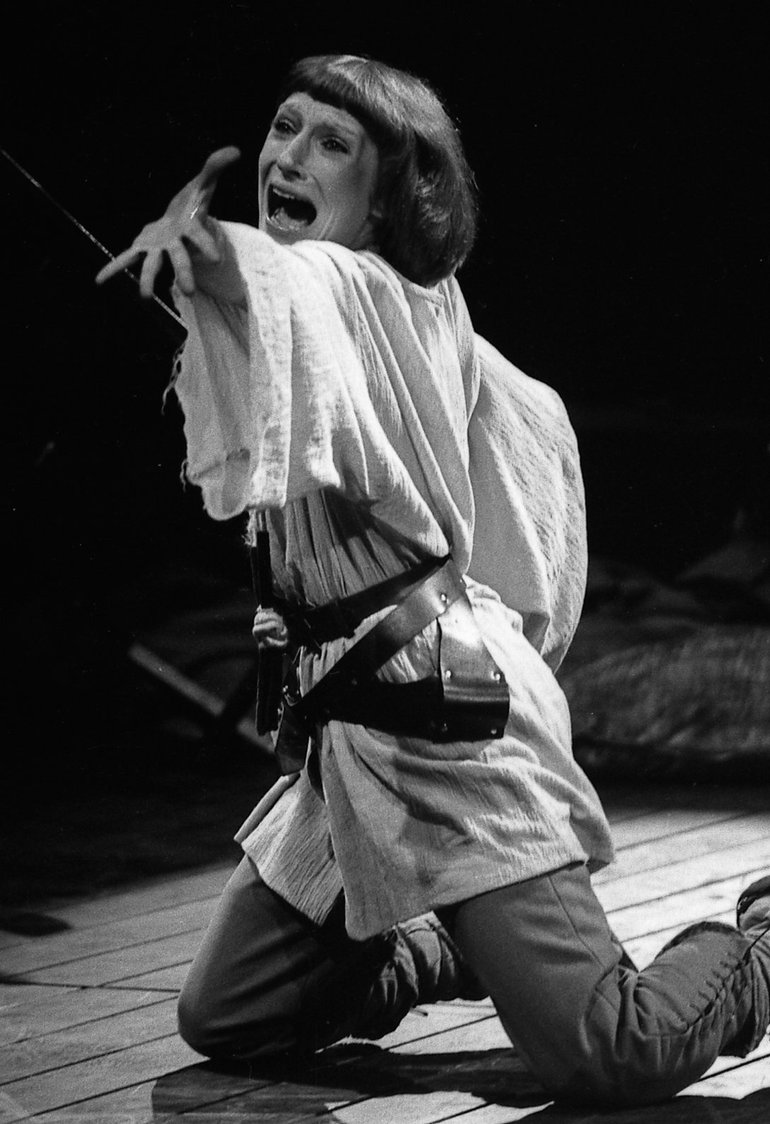 In shepherd costume (woollen trousers, long smock with wide sleeves) Joan of Arc kneels on the stage, her left arm stretched out towards us, with the palm showing, her body twisted, and her head thrown back; she is either shouting or screaming.