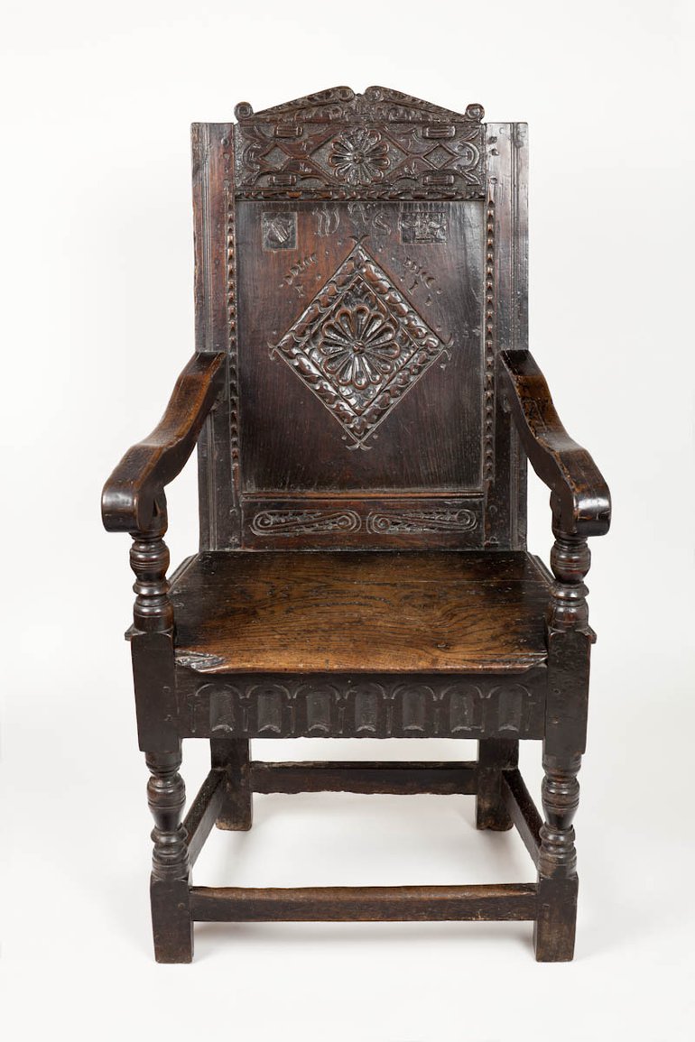 A portrait photo of Shakespeare's Courting Chair. It is a dark wood chair, with a carved back. It is of similar size and appearance to the Falcon Inn chair.