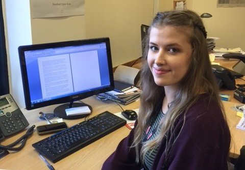 Phoebe is shown helping the marketing department as an intern. She is sat by a desk working on a computer.