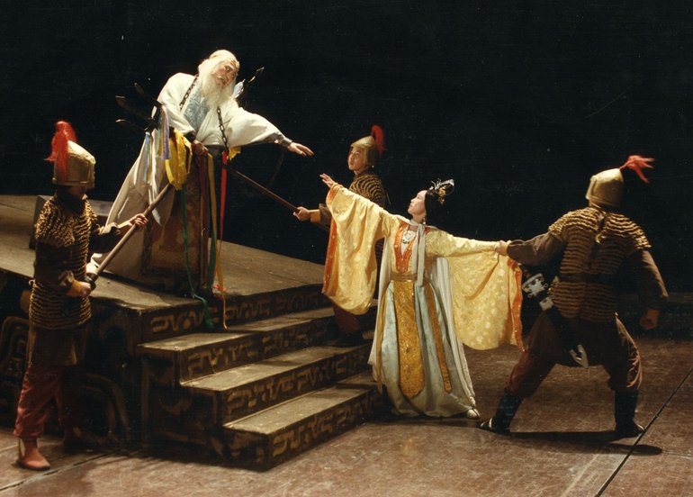 King Lear in China. Two Samurai guards point spears at Lear (long robes, white hair and beard) at the top of some steps, while another drags Cordelia away. Lear reaches out to her outstretched hand.
