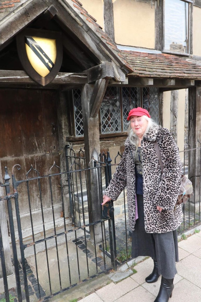 Michelle Avon standing outside Shakespeare's Birthplace, right hand on the protective rail overlooked by Shakespeare's coat of arms.