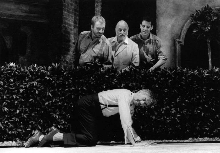 Benedick is on all fours with a hedge behind him; the three conspirators who wish him to think he is overhearing them secretly, are in fact looking at him over the hedge, unseen by him. They are all in modern dress.