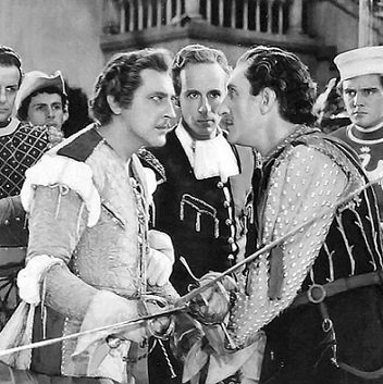 Tybalt and Mercutio face each other, their swords locked. One wears very flamboyant sixteenth-century dress of a coloured doublet with fur round the shoulders; the other a more subdued striped sleeveless jerkin.