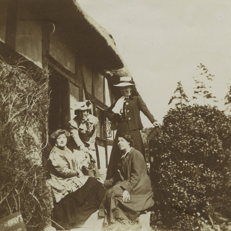 Three women sit by the cottage door, one well-dressed and two in what might be called "Edwardian rustic Best". A fourth well-dressed woman (Ellen Terry?) stands with them.