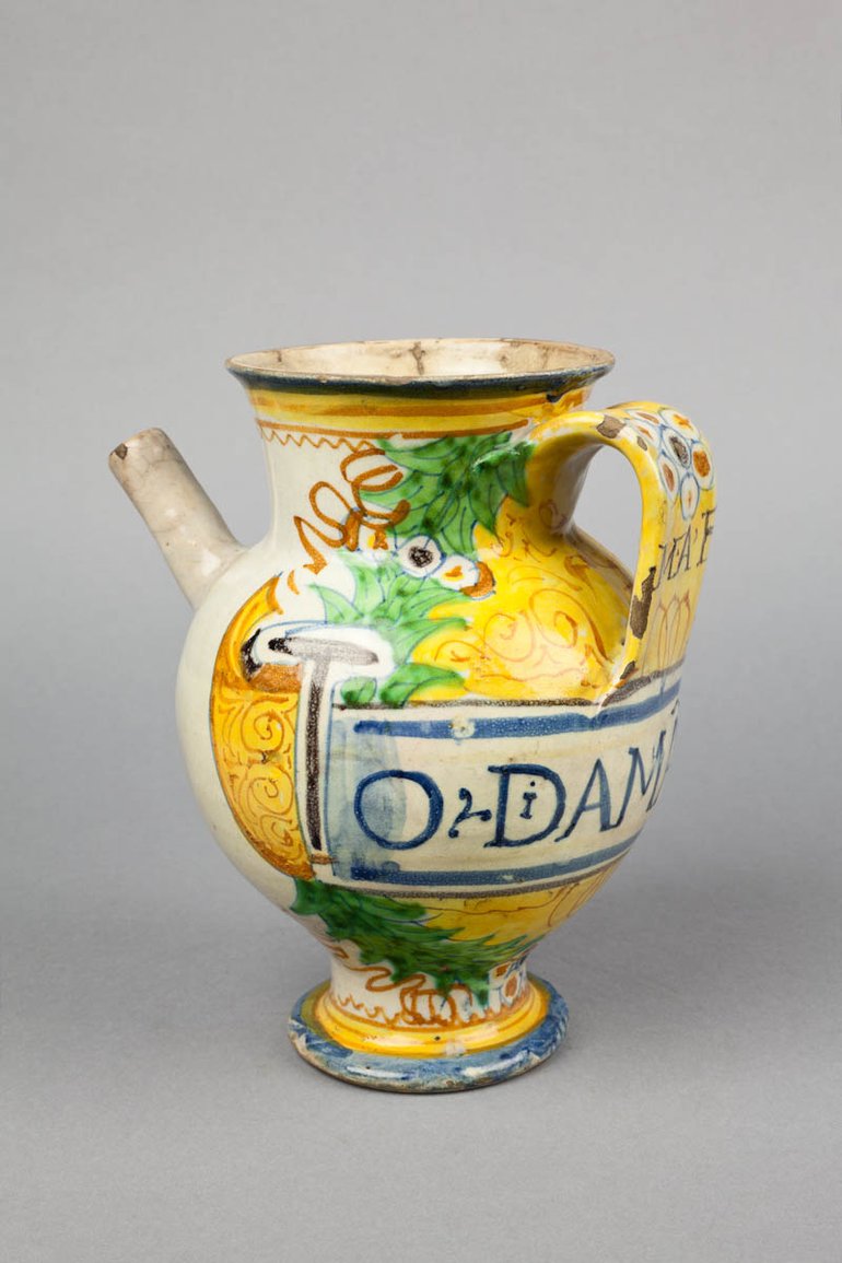 On an integral stand, this looks a bit like a teapot, with a handle and a spout; the top, however, is vase-shaped and open. It  is decorated with plant designs.