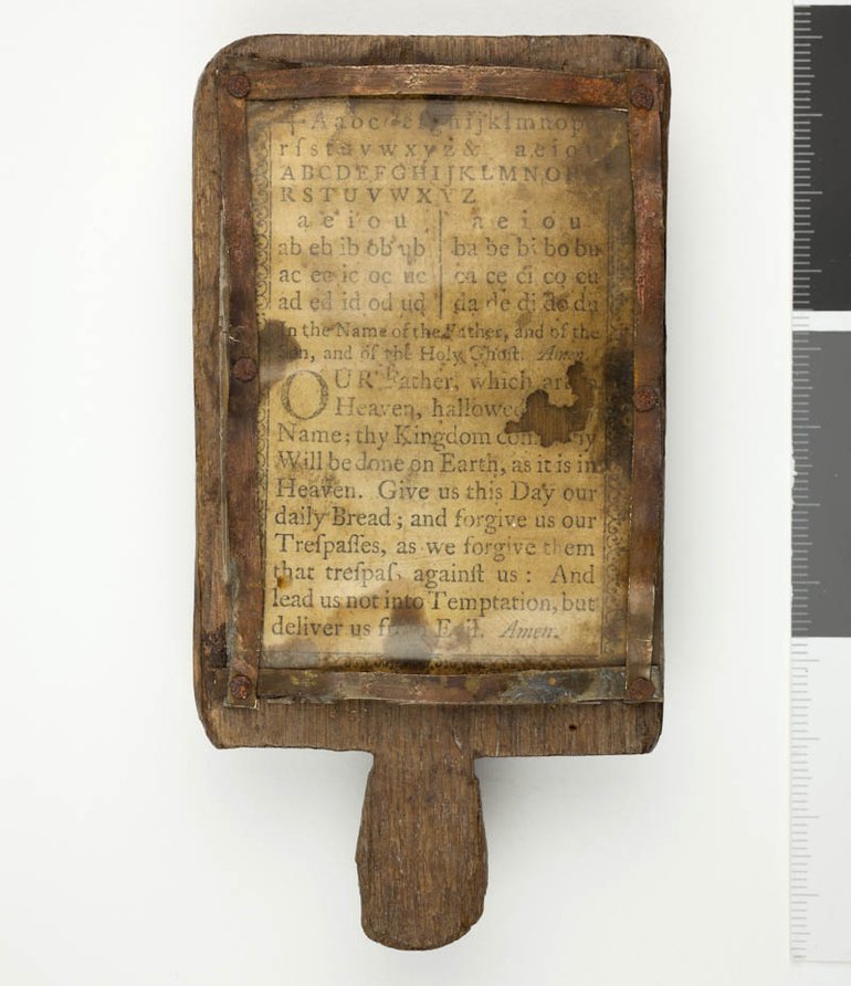The book has a rectangular wooden frame with a handle at the bottom. It encloses a horn panel which has lower snd upper case alphabets and the Lord's Prayer scratched into it.
