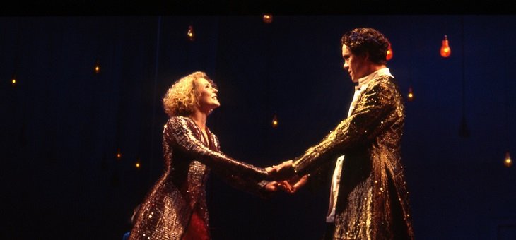 Two of the lovers hold both hands, but at arms' length. The fair-haired lady wears a red full-length dress and an embroidered gold cloak; the dark-haired man, who is a head taller, is also wearing  gold embroidered clothes.