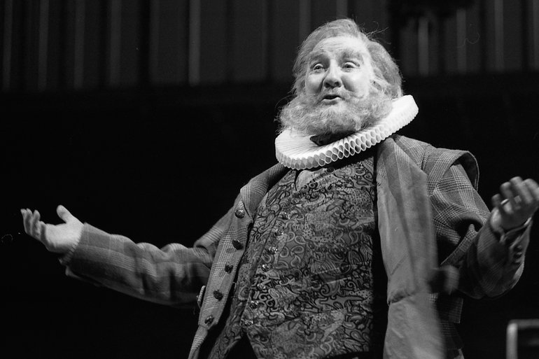Merry Wives of Windsor, RSC, 1996  A bearded Falstaff, in Elizabethan clothes with an embroidered waistcoat and a ruff stands with his arms wide, smiling.