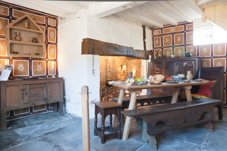 Interior of Shakespeare's Birthplace, brightly lit, showing the painted clothes on two walls imitating decorative panelling. The panel "frames" are dark brown, and the "panels" within them are light brown with even lighter geometric designs.