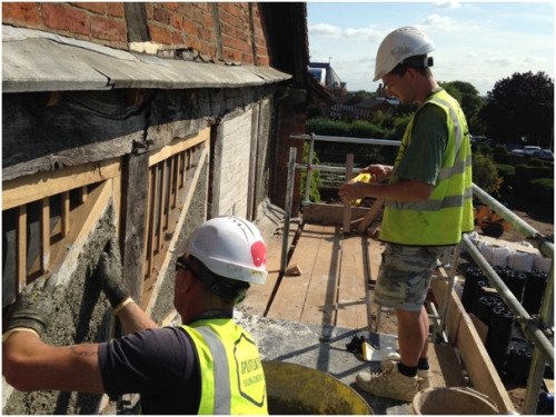 Two workmen on a scaffold platform fitting wooden frames for daubing.