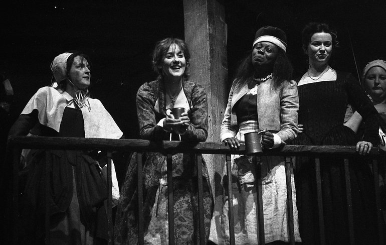 Taming of the Shrew 2003. Five ladies stand on a balcony; two of them hold drinks. All are smiling slightly, although the lady second from the left (at whom all the others are looking) is clearly laughing.