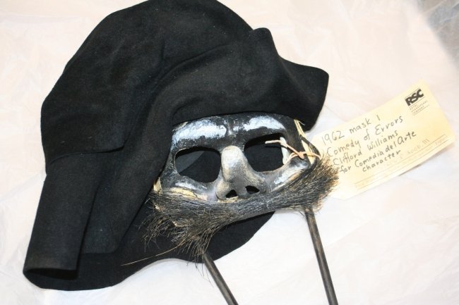 Mask worn by one of the twins in ‘The Comedy of Errors’ in 1962. A floppy black hat covering head and neck frames  a white mask with small forehead, two large eye-sockets, a stubby nose and a moustache.