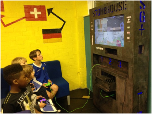 Four children working on images on a screen using hand-held controls.